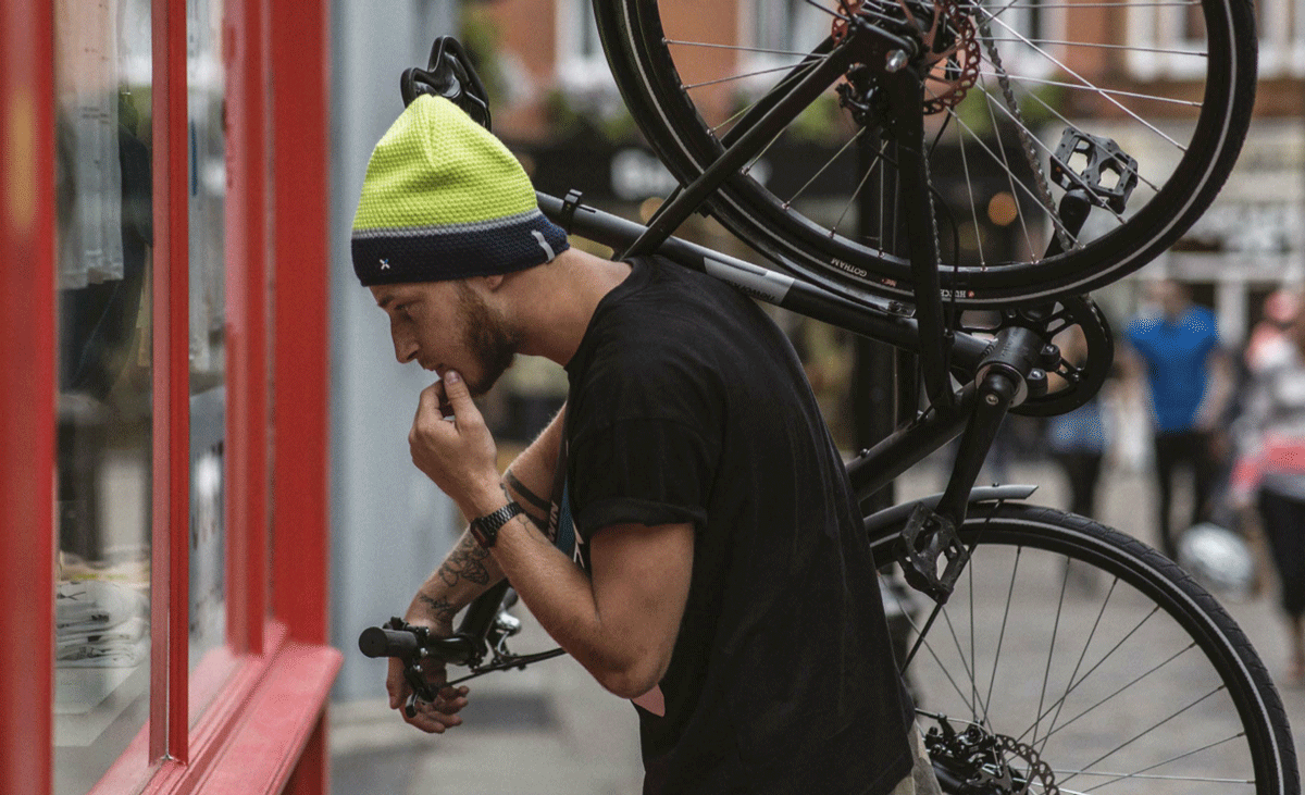 Un ragazzo davanti a una vetrina con la sua bicicletta in spalla