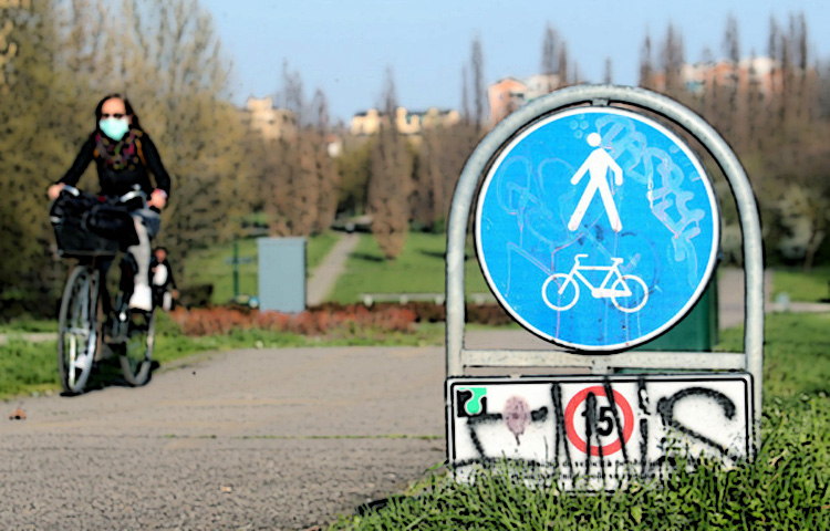 Ciclista donna pedala in un parco cittadino indossando una mascherina anti-contagio