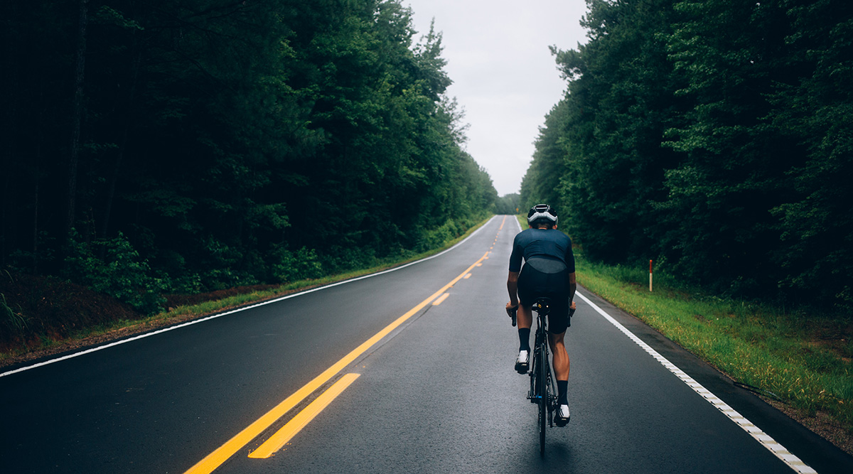 Un ciclista in sella alla bici da corsa davanti ad un suggestivo rettilineo stradale