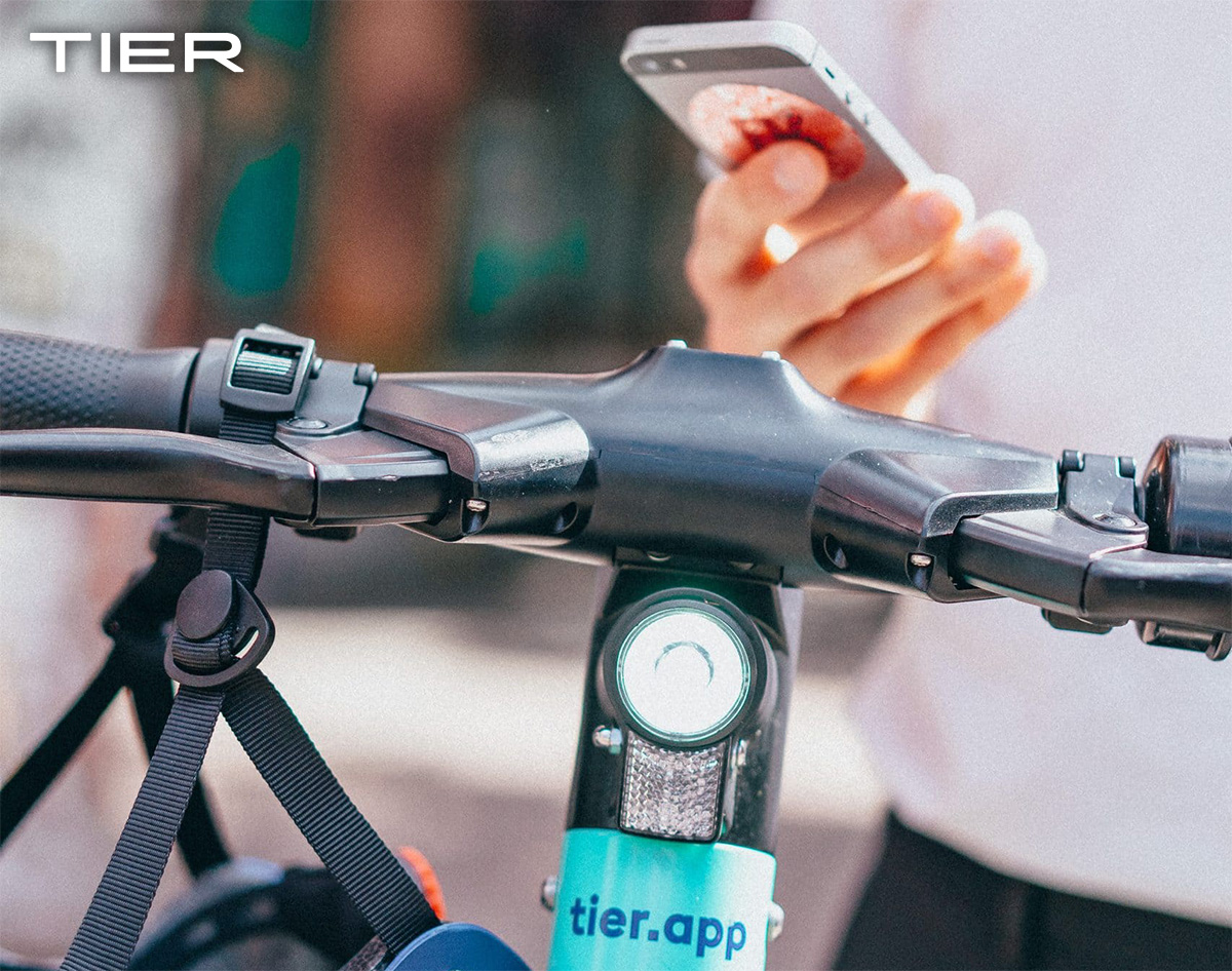 Un utente utilizza lo smartphone come navigatore mentre si sposta con un monopattino elettrico Tier